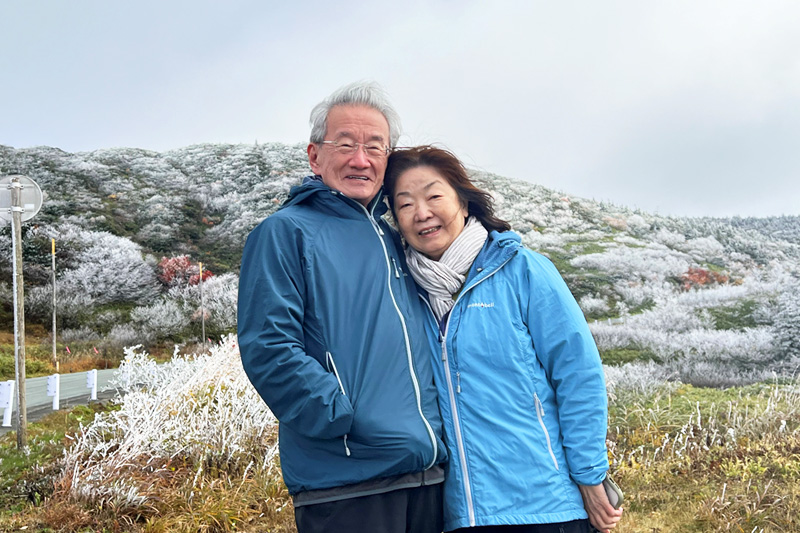 蔵王の山々を背景に立つ近森正幸相談役と奥様